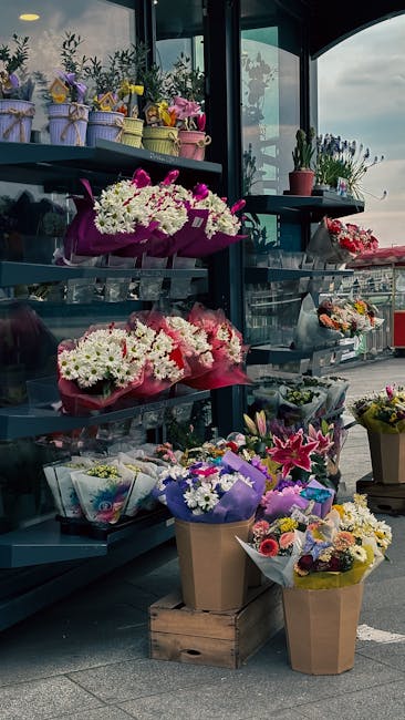 A display of colorful floral arrangements and bouquets on a multi-tiered shelf outside a flower shop near Victoria Station. The flowers include white chrysanthemums, pink lilies, purple irises, and a 
